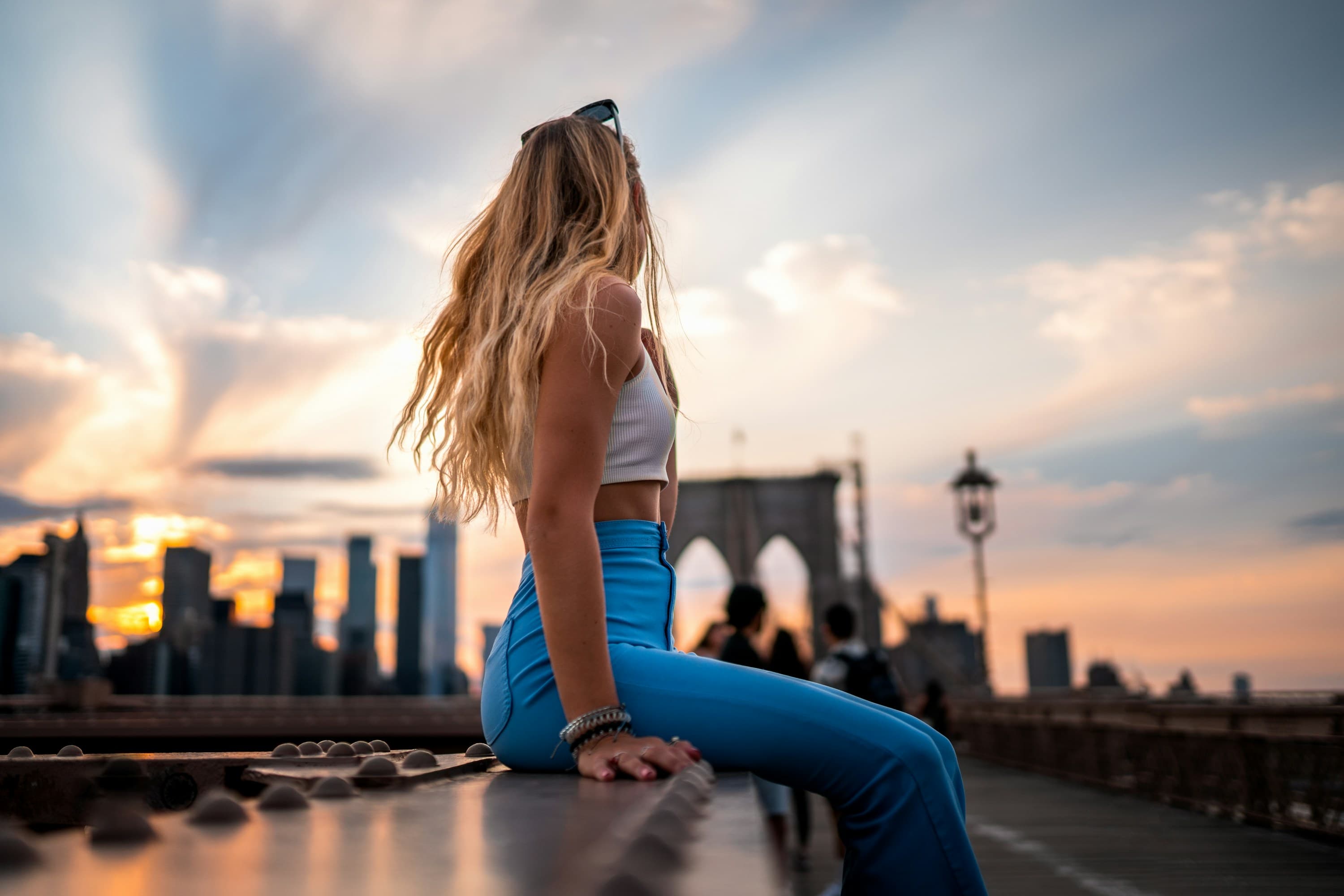 Traveler sitting on the Brooklyn Bridge with the Manhattan skyline at sunset